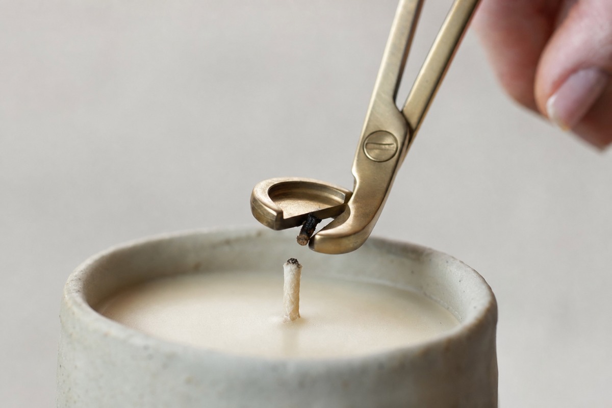 A trimmer shortening a candle's cotton wick to five millimetres before lighting