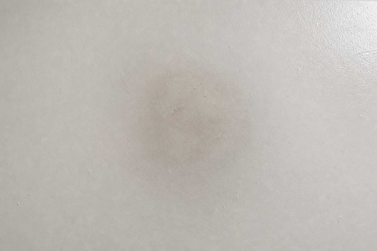 A faint grey shadow of soot on a white ceiling above where a paraffin candle once stood